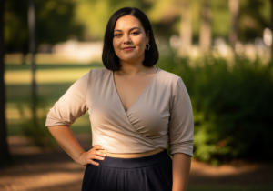 Sebevědomá plnoštíhlá žena v přírodě v příjemném oblečení, usmívá se, pozadí rozmazaná zeleň.